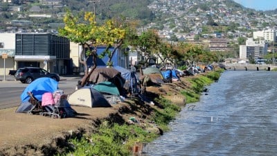 In this Thursday, June 11, 2015 photo, homeless people and their tents line a canal in Honolulu. Hours after a city crew cleared the banks of the canal, the homeless people that had been living there moved right back to the riverside, leaving some wondering whether the expense of taxpayer money was justified. (AP Photo/Cathy Bussewitz)