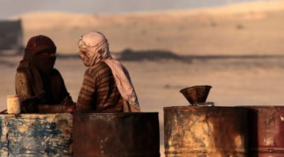 People talk as they stand next to oil barrels at a makeshift oil refinery site in al-Mansoura village in Raqqa's countryside © Hamid Khatib / Reuters